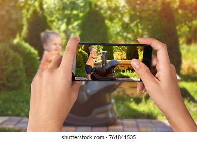 Closeup Hand Holding Phone Shooting Infant Baby Standing Near Modern Car Seat In A Park. New Born Child Traveling By Car. Child Safety On The Road.