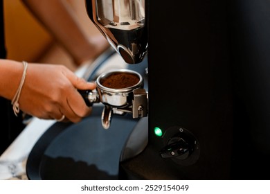 A close-up of a hand holding a portability filled with coffee grounds, positioned near an espresso machine. The machine features a sleek design with a green indicator log - Powered by Shutterstock