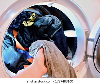 Closeup of hand holding and put washed laundry into tumble clothes dryer machine.