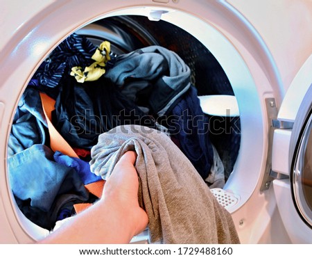 Closeup of hand holding and put washed laundry into tumble clothes dryer machine.