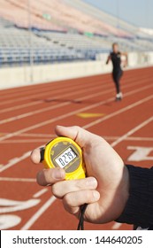 Closeup Of A Hand Holding Stopwatch With Blurred Female Runner On The Race Track