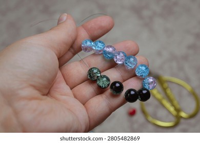 Close-up of a hand holding a string of multicolored crackle glass beads. Concept of DIY jewelry making, hobby, creative pastime, and artistic craft projects. Perfect for themes of handmade accessories.
