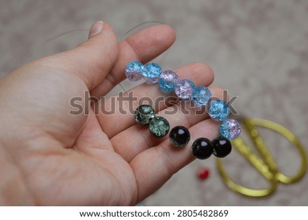 Close-up of a hand holding a string of multicolored crackle glass beads. Concept of DIY jewelry making, hobby, creative pastime, and artistic craft projects. Perfect for themes of handmade accessories.