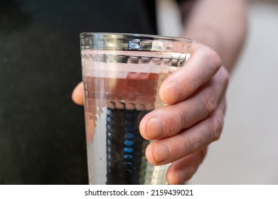 Close-up Of A Hand Holding A Tall Glass Of Water. A Mature Man In A Black Shirt Holds A Glass Of Clear Drinking Water In His Hand.
