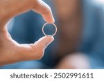 A close-up of a hand holding a thin gold ring, with a blurred background. The focus is on the ring, showcasing its shiny surface and circular shape.