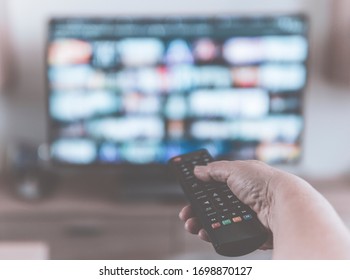 Closeup Of A Hand Holding A Tv Remote Control While Watching Shows On A Television Streaming Service - Desaturated Filter With Blurred Background