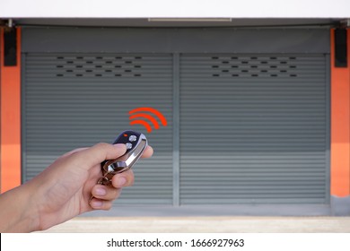 Closeup hand holding and using remote control to open the automatic shutter roller steel garage gate. Security system and wireless concept. Electronic door concept.