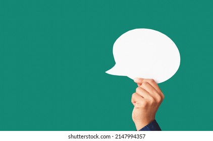 Close-up of hand holding a white speech bubble on a green background in the studio. Close-up photo. Space for text - Shutterstock ID 2147994357