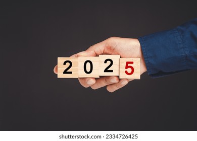 Close-up of hand holding wooden cubes with the letters 2025 against a black background. Countdown and Business Planning to 2025.
