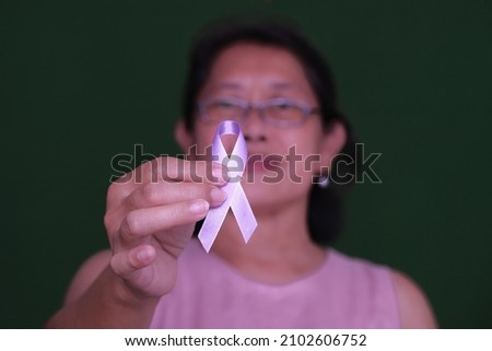 Close-up: A woman’s hand holds a pink ribbon as a symbol of breast cancer.