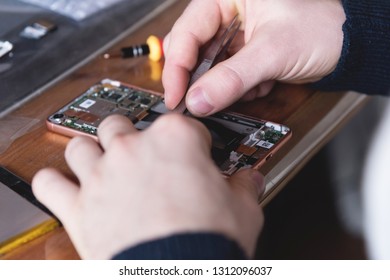 Close-up of the hand of a home craftsman repairing a disassembled smartphone. The concept of self-repair electronics at home - Shutterstock ID 1312096037