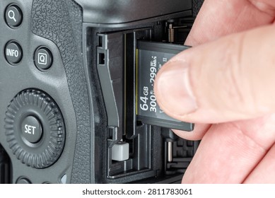 Close-up of a hand inserting a 64GB SD memory card into a professional mirrorless camera slot, macro shot of digital storage media and photography equipment interface