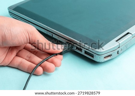 Close-up of a hand inserting a black USB cable into a laptop port. Concept of data transfer, connectivity, and hardware maintenance in a modern digital workspace