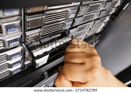 A close-up of a hand inserting a data module into a server rack, illustrating the intricacies of hardware management and technology operations in digital environments.