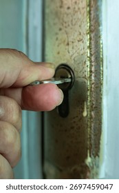 Close-up of a hand inserting a key into an old rusty door lock, symbolizing security, access, and safety concepts