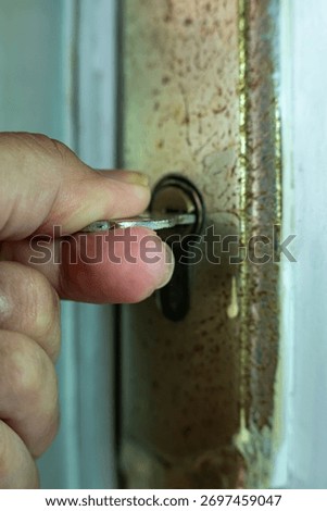 Close-up of a hand inserting a key into an old rusty door lock, symbolizing security, access, and safety concepts