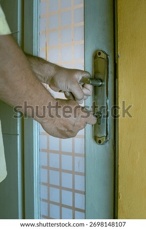 Close-up of a hand inserting a key into an old rusty door lock, symbolizing security, access, and safety concepts, in portrait 