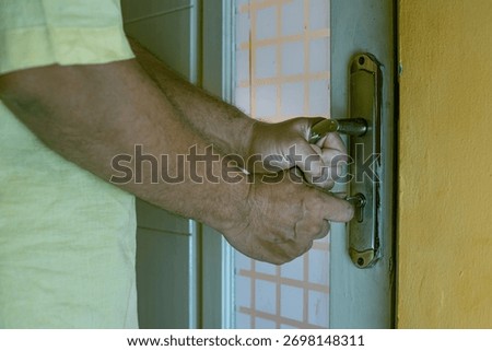 Close-up of a hand inserting a key into an old rusty door lock, symbolizing security, access, and safety concepts, landscape
