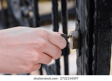 Close-up of hand inserting key and unlocking black metal gate outdoors in daylight, Security, Access control