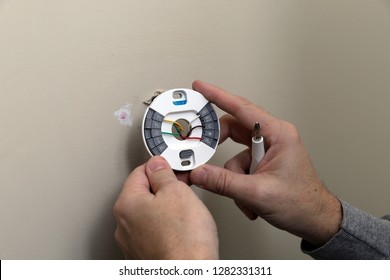 Close-up Of Hand Installing Wires And Mounting Plate For Modern Round Thermostat For Air Conditioning Unit In A House