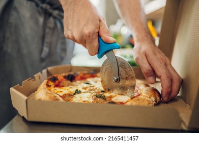 Closeup of a hand of kitchen chef cutting pizza with a pizza cutter. Man cutting pizza on a slices with special knife. Fast food nd tasty food.