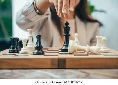 The close-up of a businesswoman’s hand making a checkmate move on a chessboard. The background shows an office setting, emphasizing the parallel between chess strategy and business acumen.