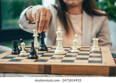 The close-up of a businesswoman’s hand making a checkmate move on a chessboard. The background shows an office setting, emphasizing the parallel between chess strategy and business acumen.