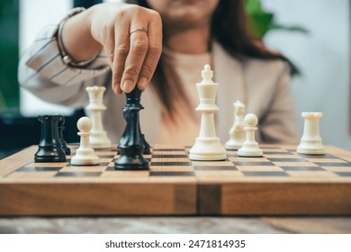 The close-up of a businesswoman’s hand making a checkmate move on a chessboard. The background shows an office setting, emphasizing the parallel between chess strategy and business acumen.