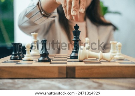 The close-up of a businesswoman’s hand making a checkmate move on a chessboard. The background shows an office setting, emphasizing the parallel between chess strategy and business acumen.