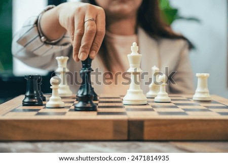 The close-up of a businesswoman’s hand making a checkmate move on a chessboard. The background shows an office setting, emphasizing the parallel between chess strategy and business acumen.