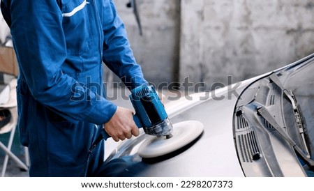 Close-up hand male mechanic wearing suit for working in garage for safety in risky work, mechanic standing using polishing machine scrub surface car that comes garage make new color.