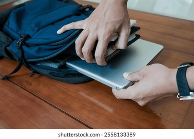 Closeup of hand man holding laptop on inside Blue backpack with books and notepad inside for student or working on the wooden table, concept back to school or working. - Powered by Shutterstock