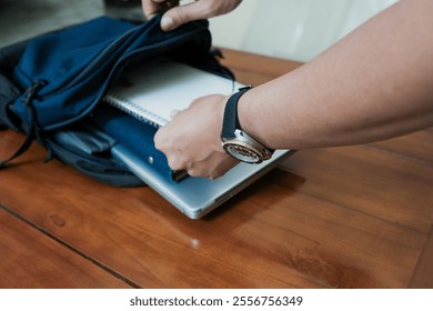 Closeup of hand man holding notepad on inside Blue backpack with books and laptop inside for student or working on the wooden table, concept back to school or working. - Powered by Shutterstock