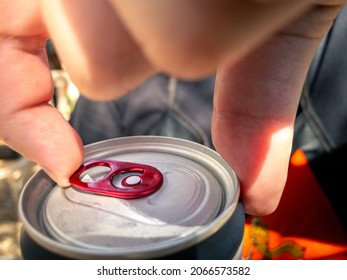 Closeup Of Hand Man Holding And Opening Pull Tab Of Soda Or Beer Can. Hands Open A Metal Aluminum Beverage Drink Cola Cans With Natural Sunlight At Outside