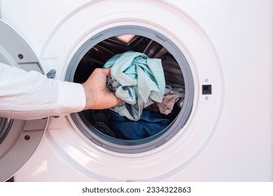 A closeup of a hand of a man putting dirty cloth into the washing machine - Powered by Shutterstock