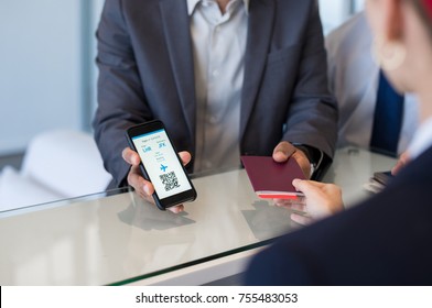 Closeup Hand Of Man Showing Flight Ticket To Staff On Phone. Hostess Checking Electronic Flight Ticket. Airport Check In Counter And Online Air Ticket.