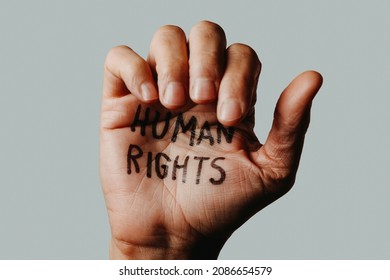 closeup of the hand of a man with the text human rights written in it, on an off-white background