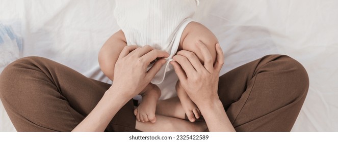 Closeup hand of mother wearing clothes after her baby changing diaper. Asian family mother’s day. Baby healthcare hygiene concept. - Powered by Shutterstock