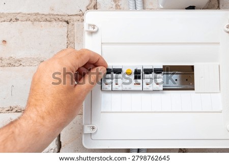 Close-up of a hand operating a modular circuit breaker in an electrical panel. Electrician flipping a circuit breaker switch in a home distribution board.