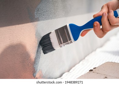 Closeup Of Hand With Paint Brush Painting Building Exterior Wall. Painting House Plinth Outside. Home Renovation