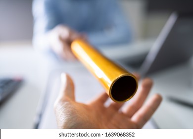 Close-up Of A Hand Passing Golden Relay Baton To Businessman