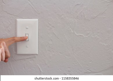 A Closeup Of A Hand Or Person Turning Or Flipping A White Light Switch Off On A Gray Wall Background, Energy Conservation Connection Or Disconnection Or Waste Concept, Horizontal Shot, Copy Text Space