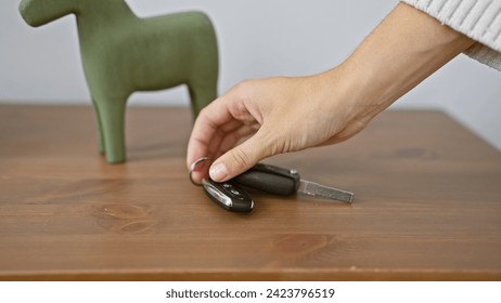 Close-up of a hand picking up car keys on a wooden table with a decorative object in a room. - Powered by Shutterstock