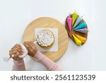 Closeup hand piping white cream on a sponge cake, creating a decorative pattern on the top of a round, light-colored cake that