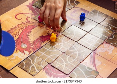 Close-up Hand Playing Board Game Similar To As Tsuro. Table Game Or Game Night With Friends. Hand Control Multi-colored Figures. Movement, Selective Focus.