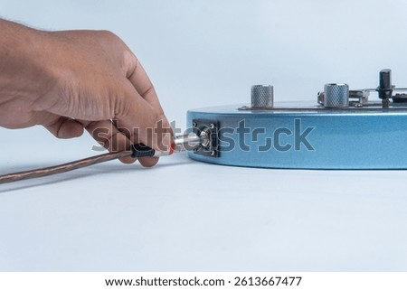 Close-up of a hand plugging an audio cable into the body of a blue electric guitar. Isolated on a white background. Perfect for music, instrument setup, or sound equipment visuals.