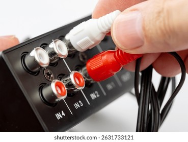 Closeup of a hand plugging in red and white RCA cables into the audio input ports on modern device, macro closeup detail view, analog connection sound mixer stereo system, connecting cables
