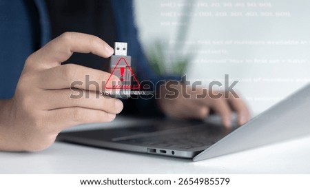 Close-up hand plugging USB with system warning alert, cybersecurity threat, malware infection risk, data breach prevention concept in digital workplace.