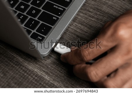 Close-up of Hand Plugging White USB C Cable Connector into Laptop Port on Dark Wooden Desk
