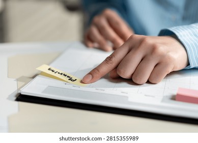 Close-up of a hand pointing to a sticky note on a planner during business scheduling, illustrating task management, project planning, productivity, organization, deadline tracking and time management.